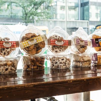 Assorted cookies in clear plastic containers on a wooden shelf by the window.