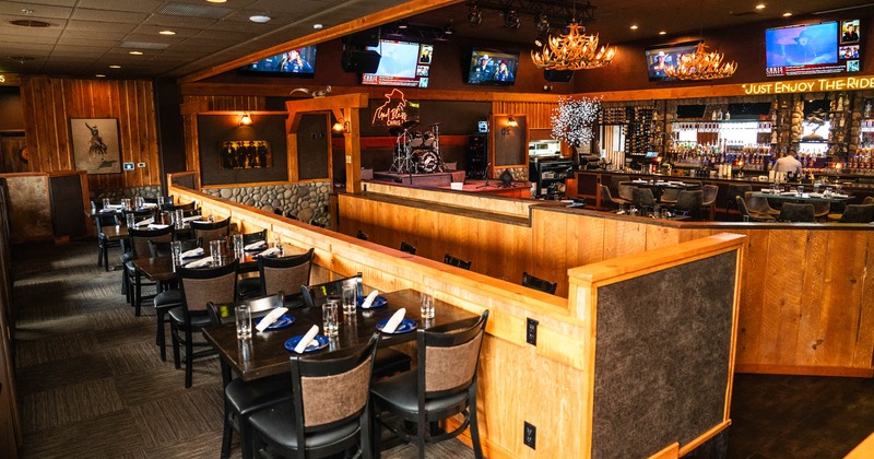 Interior, tables with chairs ready for guests, central space and bar in the back, wooden details