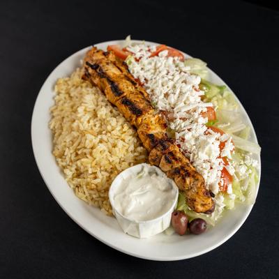 An overhead view of a chicken souvlaki served over rice and chopped salad with a side of tzatziki.