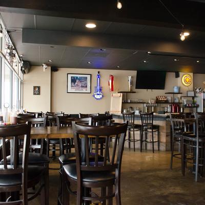 Interior featuring wooden tables and high chairs, with a small bar at the back.