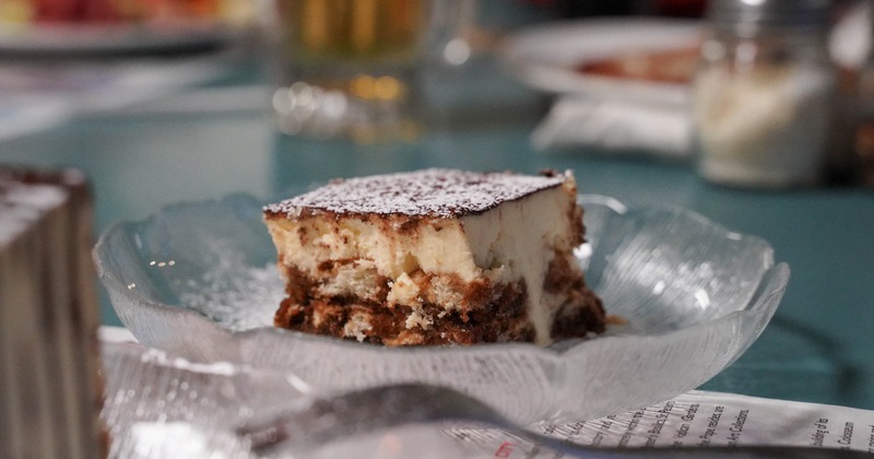 Tiramisu slice dusted with powdered sugar served on a glass plate