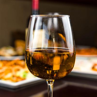 Close up of a glass of white wine, with food in blurred background.