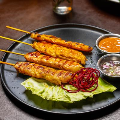Chicken satay served with peanut sauce and garnishes.