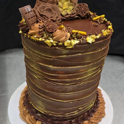 Tall chocolate cake with textured gold accents, topped with chocolate decorations.