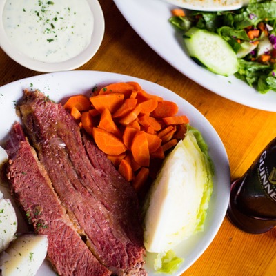 A large slab of corned beef plated next to boiled potatoes, a quarter of a cabbage and cooked carrots