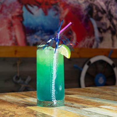 Blue cocktail in tall glass with lime garnish.