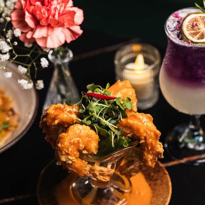 Fried shrimp surrounded by a cocktail, flowers, and a candle.