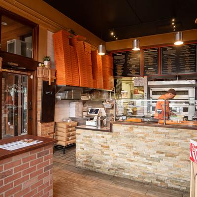 Interior of a pizza place with an oven, pizza boxes, and menu boards.