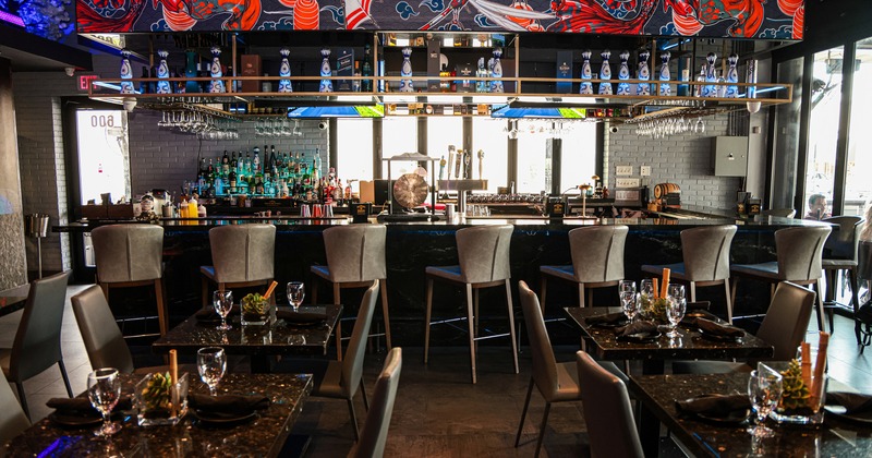 Modern restaurant interior, bar with upholstered stools, and dining area with tables set for guests
