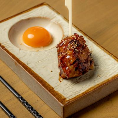 Japanese chicken meatball served on a skewer with a side of raw egg yolk.