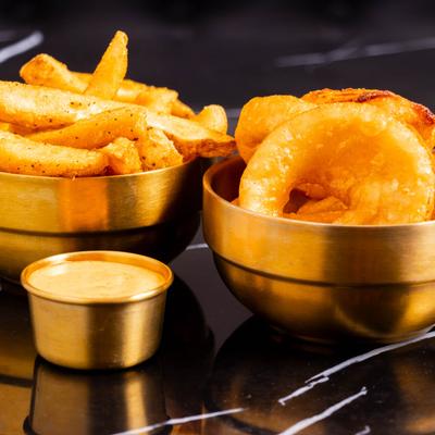 A bowl of fries and a bowl of onion rings with dipping sauce.