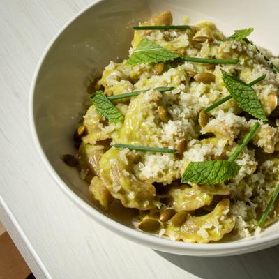 Pasta dish topped with mint leaves, pumpkin seeds, grated cheese and chives.