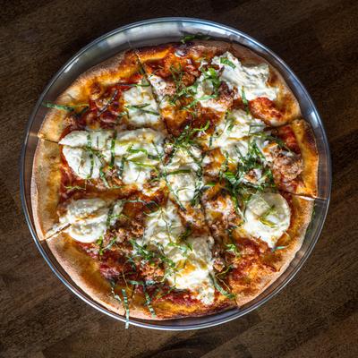 Sausage and ricotta pizza with hot honey drizzle and basil garnish.
