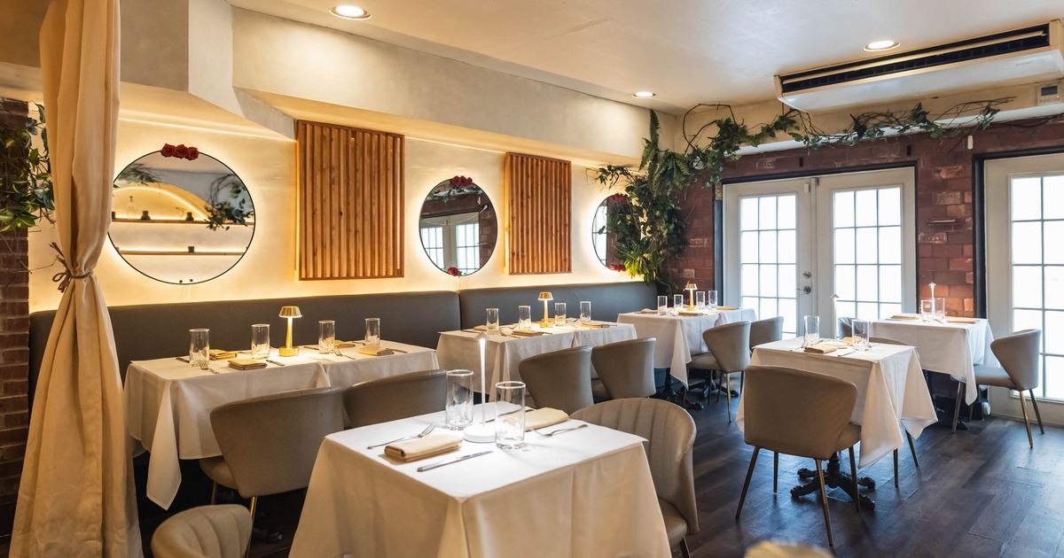 A stylish restaurant interior with white tablecloths, beige chairs, round mirrors