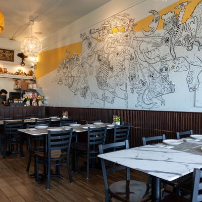 Dining room with tables, chais, counter, pendant lights and mural art on the wall.