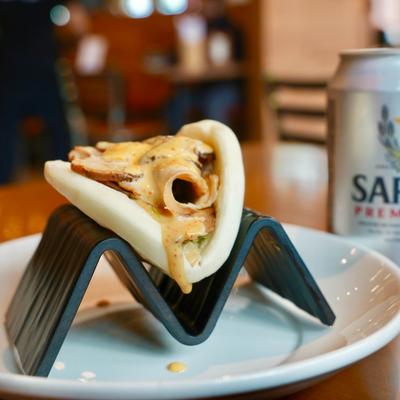 A bao bun rests on a black holder next to Sapporo beer.