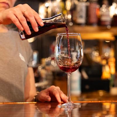 A bartender pouring a glass of red wine from a pitcher.
