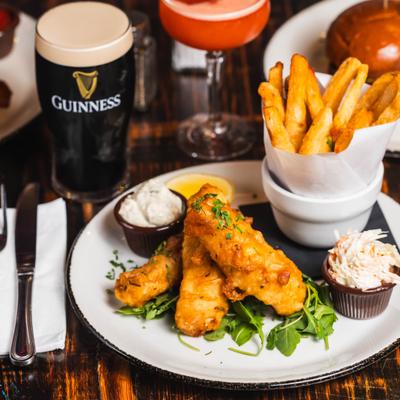 Fish and chips served over arugula with tartar sauce, coleslaw, and drinks.
