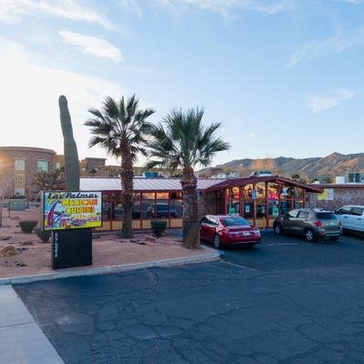 Exterior, restaurant building with palm trees and parked cars.
