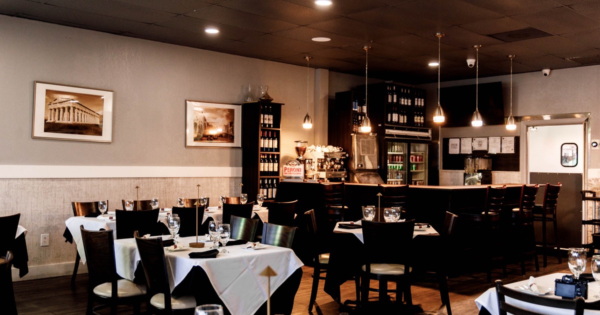 Cozy restaurant interior with tables set with white tablecloths and a bar in the background