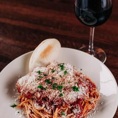 Spaghetti with marinara sauce, grated cheese, and bread roll beside a glass of red wine.