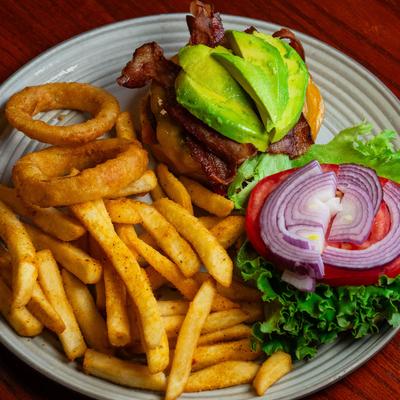 California burger served on a plate with fries and onion rings.