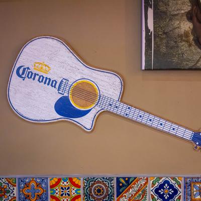 Guitar-shaped sign with a Mexican beer logo on a wall.