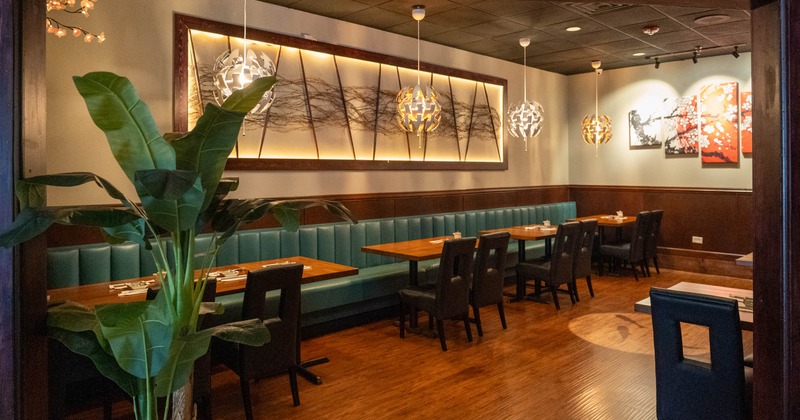 A modern restaurant interior with teal banquette seating, wooden tables, pendant lights, and abstract artwork
