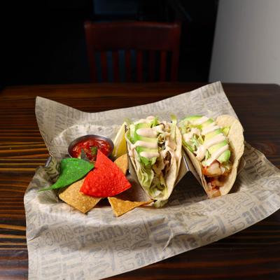 Two grilled fish tacos with corn chips.