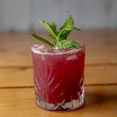 A purple cocktail on the rocks, garnished with a mint sprig.