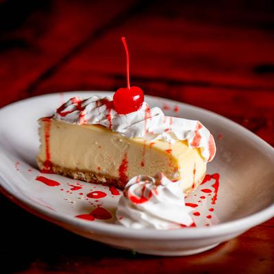 A slice of cheesecake topped with whipped cream and a cherry.