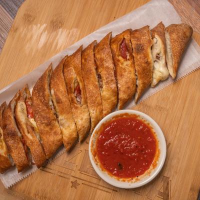 Sliced pepperoni stromboli with marinara sauce served on a wooden board.