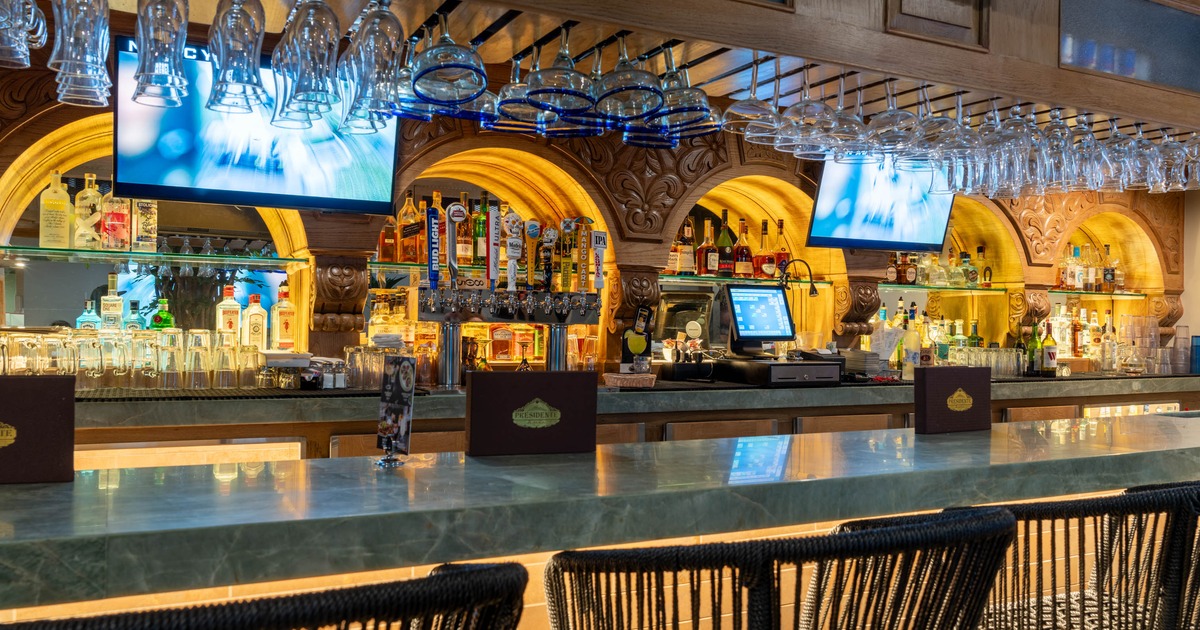 A bar with a marble counter, hanging glasses, liquor bottles, and beer taps