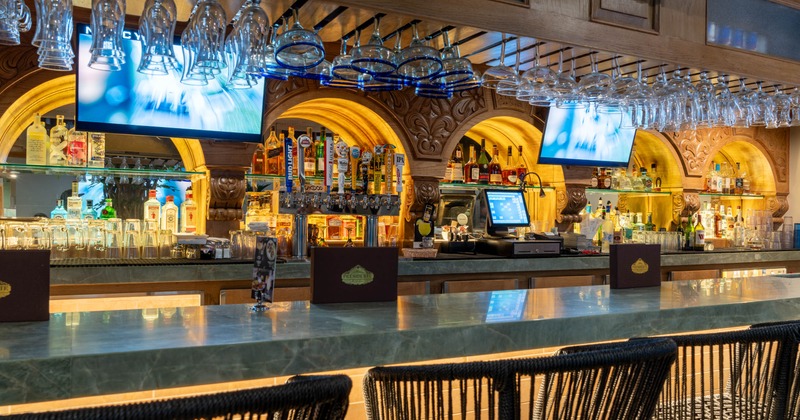 A bar with a marble counter, hanging glasses, liquor bottles, and beer taps