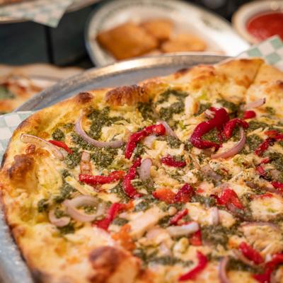 Pizza with roasted chicken, mozzarella, pesto, red onions, and red peppers.