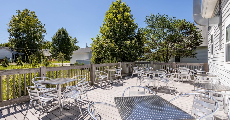 Exterior, patio, low wooden railing, wooden flooring, aluminum tables and chairs