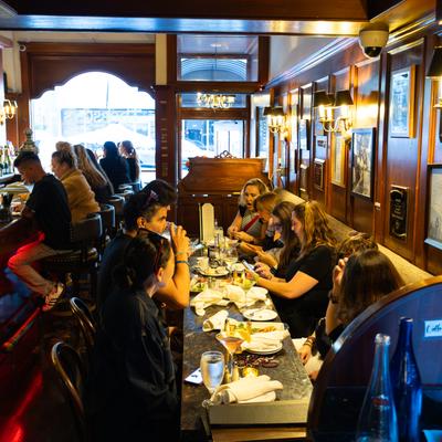 People dine and drink at a long table indoors.