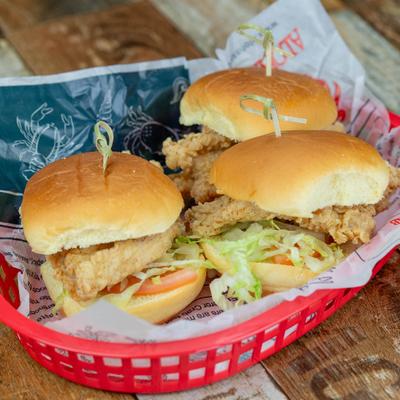 Chicken sliders topped with lettuce, tomatoes, and pickles in a red basket.