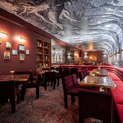 Room with red seating, marble tables, vintage decor, black-and-white mural on the ceiling.