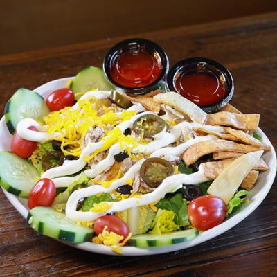 A salad with pulled chicken, lettuce, jalapenos, cheese, cucumbers, served with two sauces.