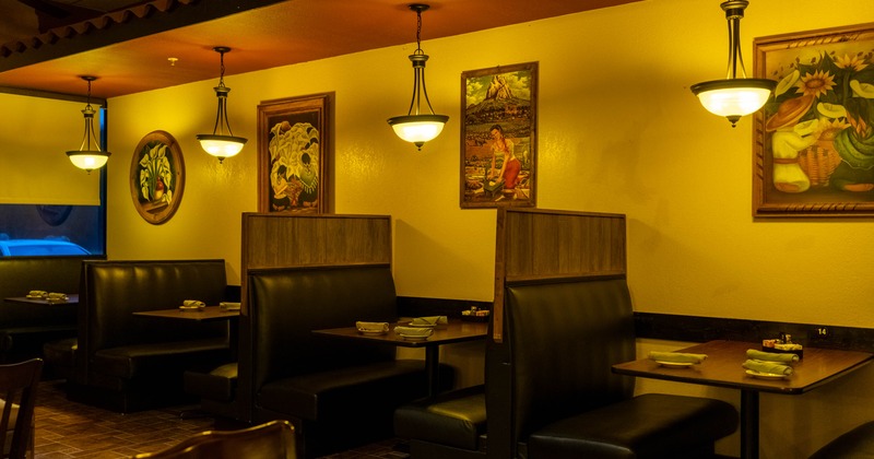 Interior of a warmly lit restaurant with booths and framed artwork on yellow walls