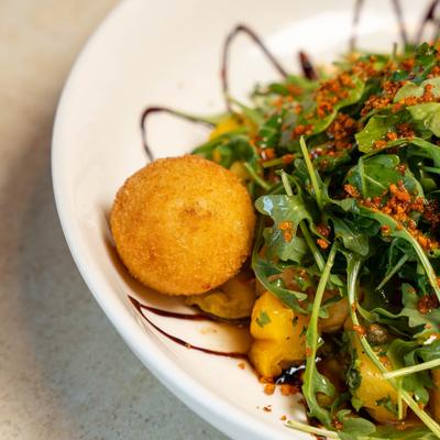 Crispy fried cheese ball served with arugula salad, peppers, and balsamic drizzle.