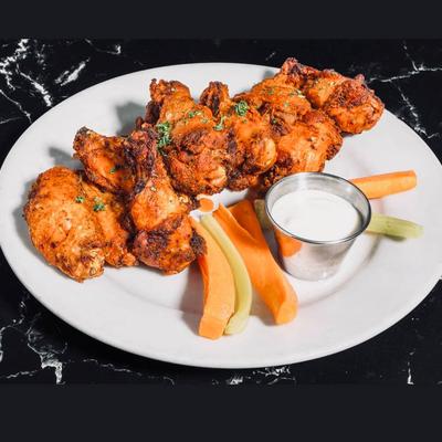 Buffalo wings served on a white plate with celery, carrots, and ranch.