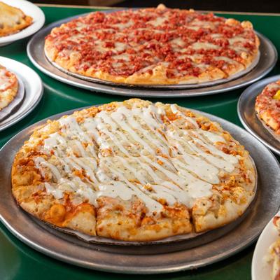Assorted pizzas on round metal trays are displayed on a table.