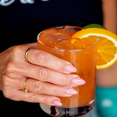 Hand holding a orange cocktail served on ice with citrus wheels.