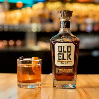 A bottle of whiskey beside an Old Fashioned cocktail on a table