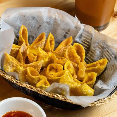 Crispy wontons in a basket on wooden table.