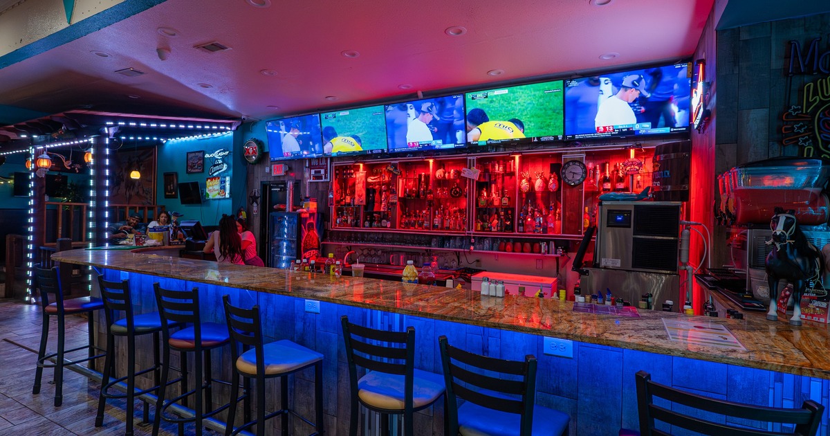 Bar area with ambient neon and red backlighting, counter and multiple TV screens