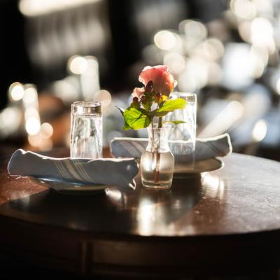 Interior, a table set with a rose in a vase, two plates with napkins, and two glasses.