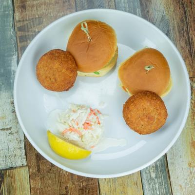 Crab cake served with coleslaw, a lemon slice, and two sliders.